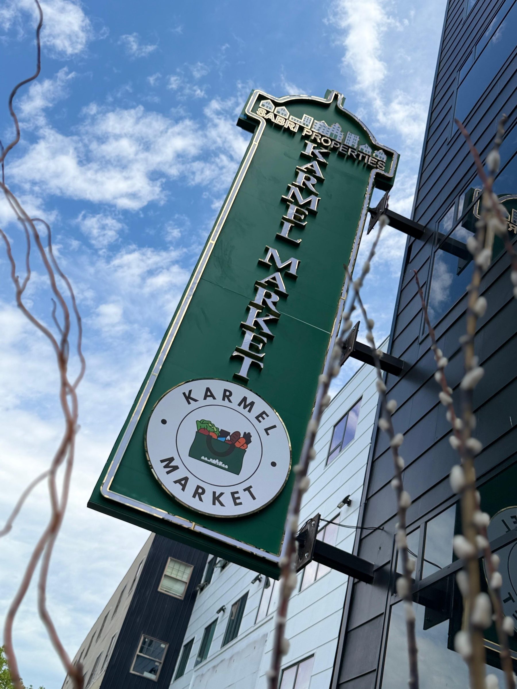 The green Karmel Market blade sign on the building exterior along Pleasant Avenue